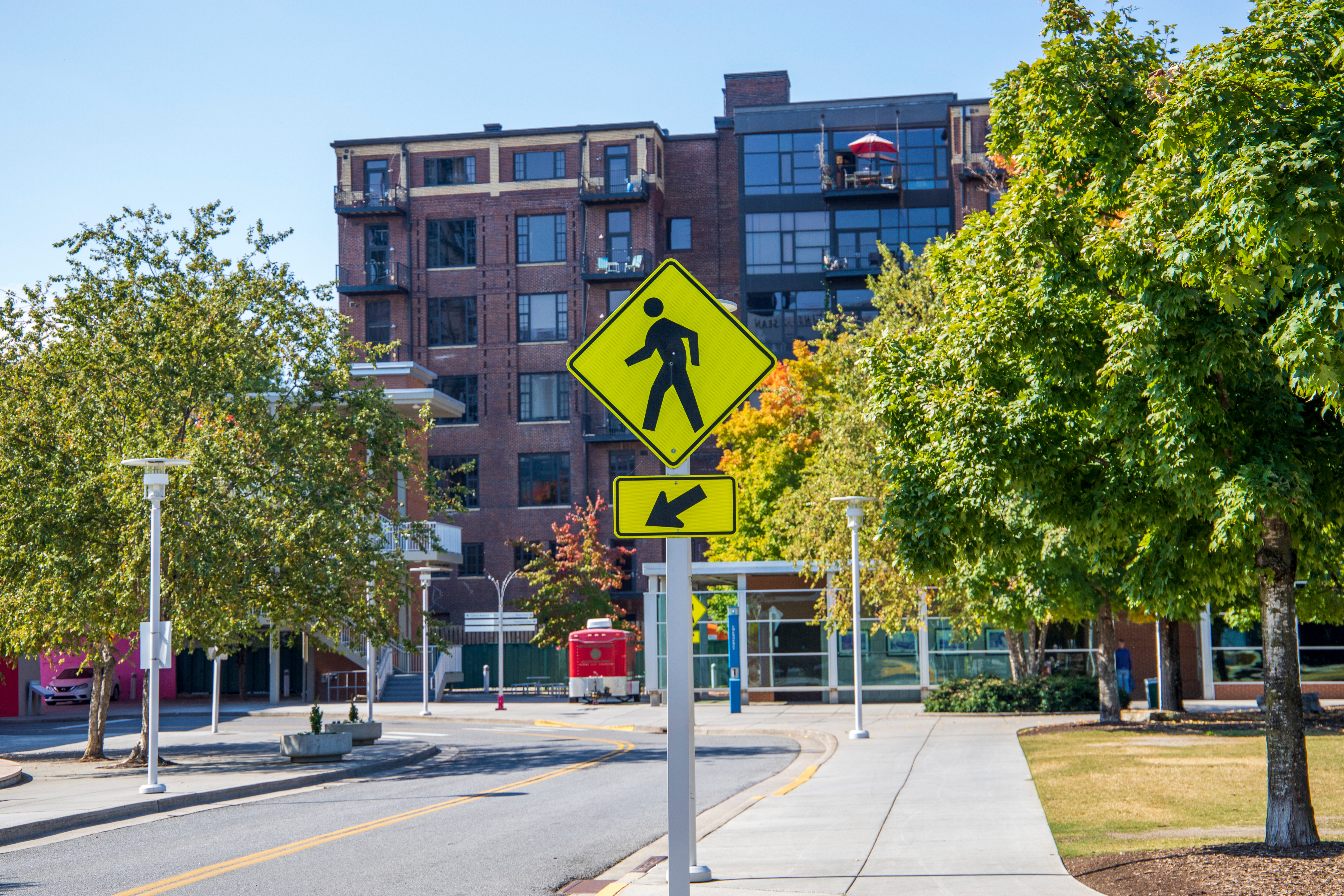 yellow crosswalk sign between trees and in front of brick building. Image Credit: AdobeStock_539045487